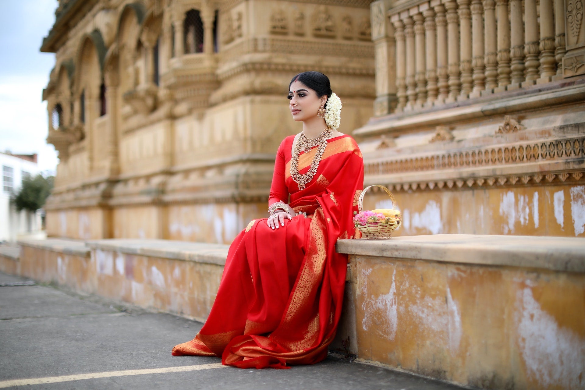 Beautiful Indian lady sitting in front of a historic Indian palace featuring a pure silk saree.